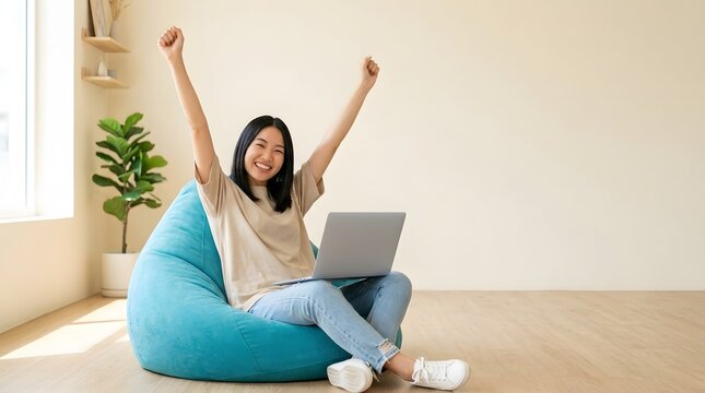 Joyful woman raising arms while sitting with a laptop on a beanbag
