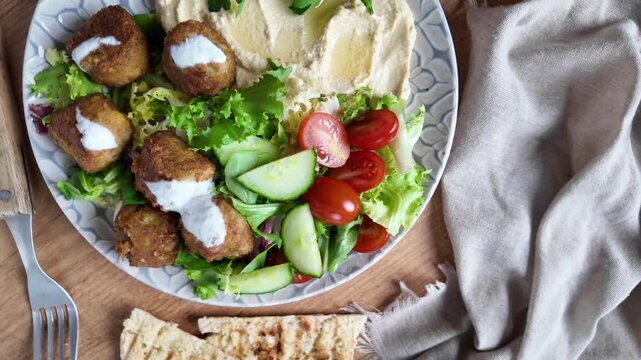 Traditional falafel served with hummus and fresh salad on wooden table