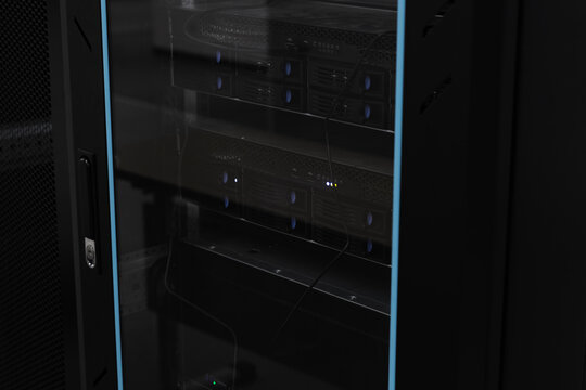 Glass-doored server rack housing rack servers and cabling. Dimly lit IT equipment conveys technology, connectivity, security and professional network infrastructure