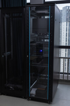 Glass-doored server rack in a modern office data center housing rack servers, monitor and cabling. Dimly lit IT equipment conveys technology, connectivity and professional network infrastructure