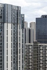 Fototapeta premium A cluster of tall residential and commercial high-rise buildings showing dense urban architecture, concrete facades, repeating windows and balconies under a cloudy sky in a modern city. Wuhan, China