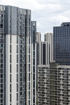 A cluster of tall residential and commercial high-rise buildings showing dense urban architecture, concrete facades, repeating windows and balconies under a cloudy sky in a modern city. Wuhan, China