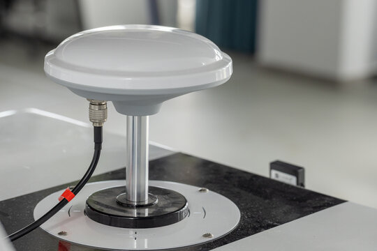 White dome GPS antenna mounted on a metal pedestal with a coaxial cable connection, photographed in a clean laboratory setting. Suitable for technology, navigation, communication and testing illu