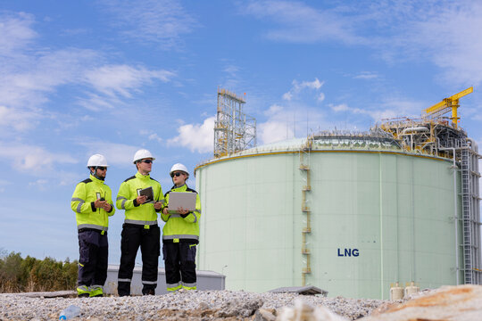Team of engineers working together on the construction site of a liquefied natural gas facility with bright blue skies above