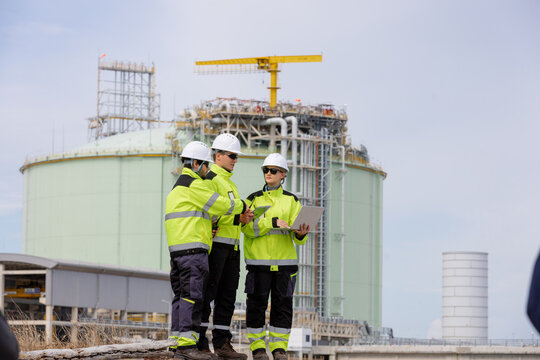 Team of engineers wearing safety gear working together on a construction site with an industrial building in the background