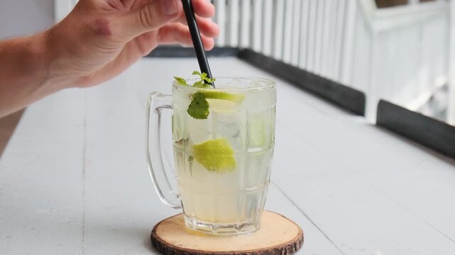 Man drinking mint lime refreshing iced drink lemonade in glass mug with a straw in Phuket, Thailand. Mojito mocktail. Summer refreshment, healthy drink and tropical lifestyle concept