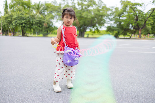 Adorable Asian Girl Playing with a Rainbow Slinky Spring Toy Outdoors,A cute young Asian girl standing in a park, holding and playing with a vibrant, colorful rainbow-colored slinky spring toy.