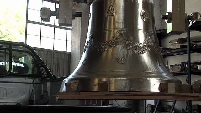Worker Hand Moving Big Shiny Bronze Bell Suspended In Traditional Foundry - 4K