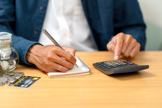 Close up hand of man point to calculator on table during work with writing on notebook.