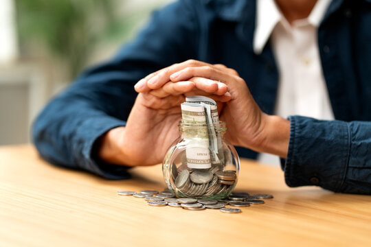 Close up man hands cover over jar of bank and coin in concept of collect income for payment in the future.