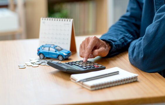 Close up hand of man using calculator on table during work and car model also put on table in concept of concern income or money to buy car.