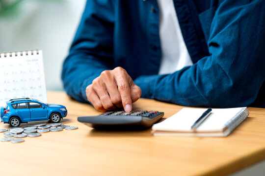 Front view hand of man using calculator on table during work and car model also put on table in concept of concern income or money to buy car.