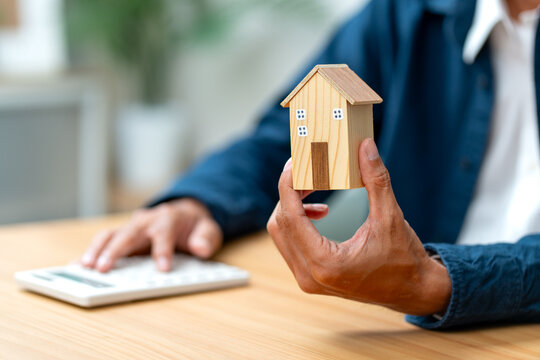 Close up man hands hold house model with other hand use calculator in concept of collect income for home payment in the future.