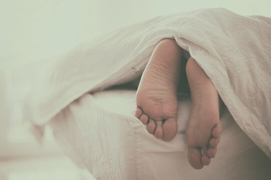 Close-up  of a Man's feet sticking out of the end of a duvet on a bed