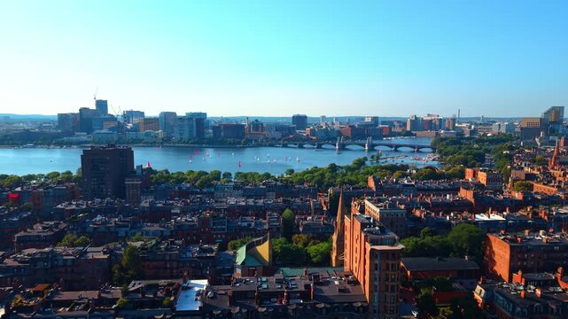Flight over the historical neighborhood with lush greenery at the river waterfront. Approaching the Charles River with multiple sailboats on.