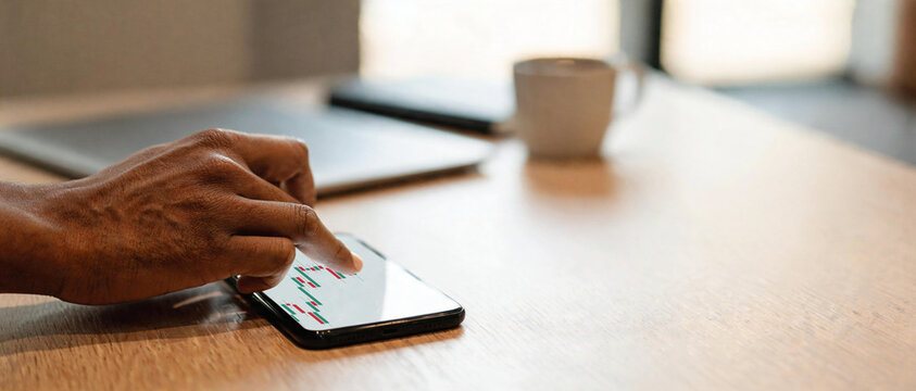 Primer plano de mano oscura interactuando con un gr&aacute;fico financiero de velas en la pantalla blanca de un smartphone sobre escritorio. Concepto de inversi&oacute;n m&oacute;vil, trading y an&aacute;lisis.