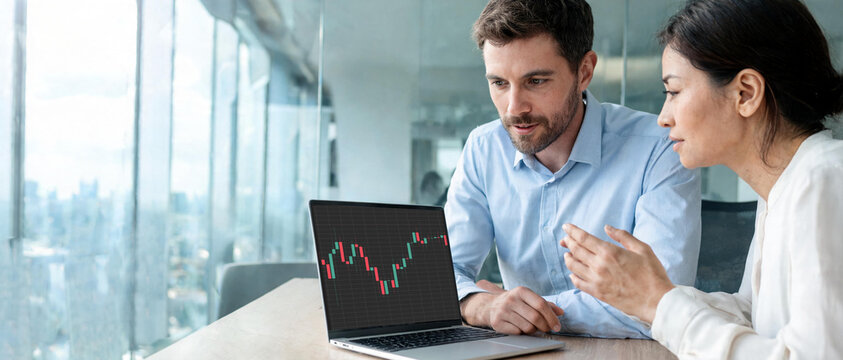 Socios comerciales analizando un gr&aacute;fico t&eacute;cnico de trading en una laptop dentro de una moderna oficina corporativa. Concepto de trabajo en equipo, inversiones y finanzas corporativas.