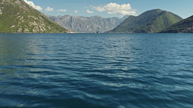 aerial forward tilt up reveal of a white sailing yacht under sail on the bay of kotor passing our lady of the rocks island with a distant cruise ship and steep grey mountains, montenegro