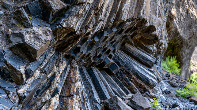 Columnar basalt formation cross-section revealed at cliff face, hexagonal cooling crack geometry in dramatic sidelight, volcanic geology, prismatic jointing pattern, igneous rock structure, geologic
