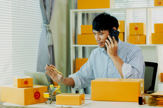 Enthusiastic male online store owner writing purchase log during smartphone e-commerce call.