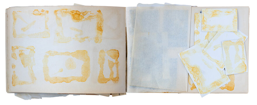 Open vintage photo album with missing photographs, yellowed glue marks and loose mounting papers on white