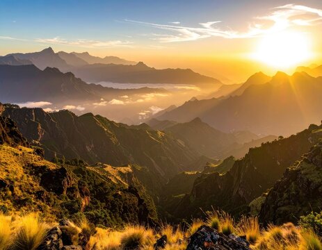 Golden sunrise illuminates a vast mountain range with layered peaks and misty valleys.