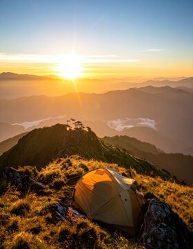 A tent is pitched on a grassy mountain ridge as the sun rises over a misty valley.