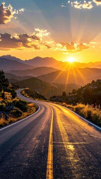 A winding road stretches towards a vibrant sunset over mountainous terrain.