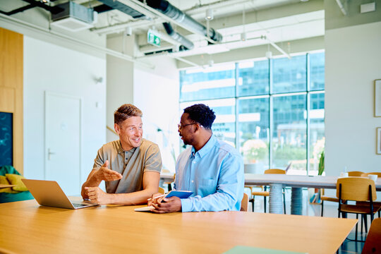 Business colleagues discussing work, collaborating on a project with a laptop during a meeting in a contemporary office setting