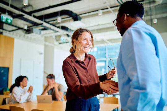 Business partners forming an agreement and connection shaking hands, smiling in a modern office meeting space