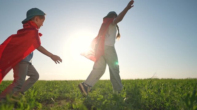 Boy plays superhero chasing girl fast. Running across green field outdoor joy. Summer child playing superhero dream. Girl laughs enjoying outdoor summer. Boy happy superhero running with girl playing.