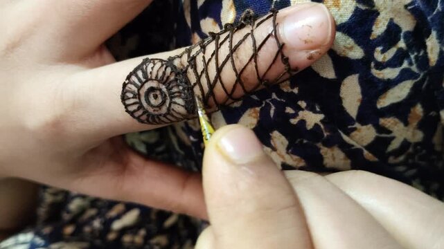 Close up video of a mehndi artist applying an intricate henna design on a finger using a henna cone, showcasing traditional body art.