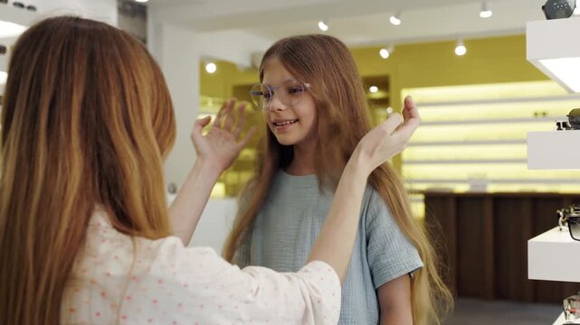 Mother helping her daughter choosing glasses in an optic store