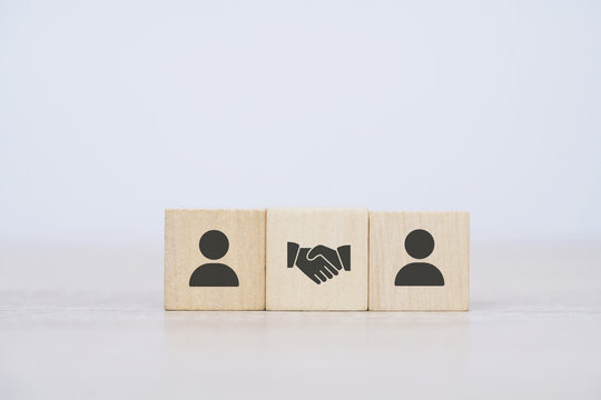 wood cube block with handshake agreement icon symbol between two person cubes, concept of business, deal, partnership or cooperation between parties and sales according to business goals.