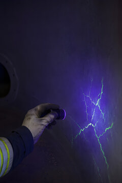 Worker hand holding UV black light flashlight revealing glowing fluorescent cracks on dark metal surface during non-destructive testing quality control industrial inspection