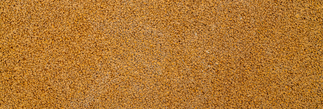 Close up texture of golden yellow fine gravel rubber surface for outdoor flooring, landscaping and park design concept