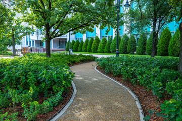 Obraz premium Curved walking path through manicured green park with trees and hedges in summer city, urban landscape design concept
