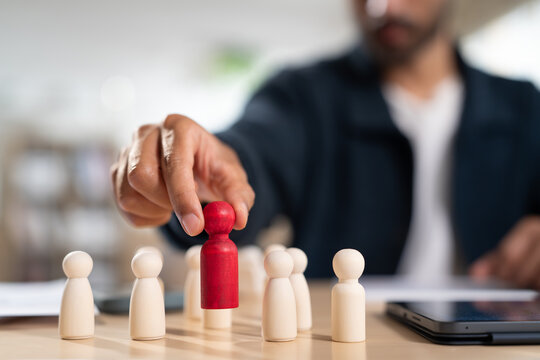 Close up of entrepreneur or businessman selecting unique red figure from plain wooden dolls on table. Corporate management choosing outstanding team leader supervisor. strategy and planning concept