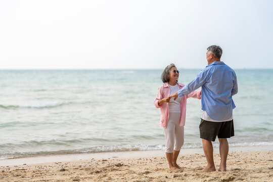 Happy Senior Asian Couple Dancing Joyfully on the Beach, Retirement Travel Lifestyle