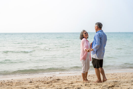 Happy Senior Asian Couple Dancing Joyfully on the Beach, Retirement Travel Lifestyle