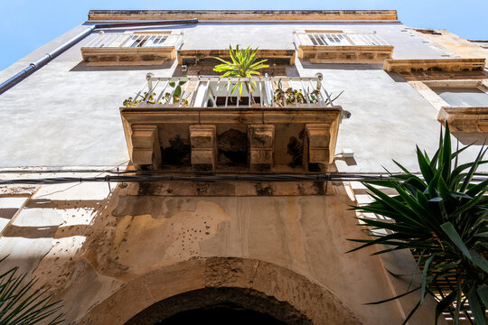 A view looking straight up from below at an old building, with palm trees at the bottom, an arch and symmetrical balconies, all brightly lit by the sun