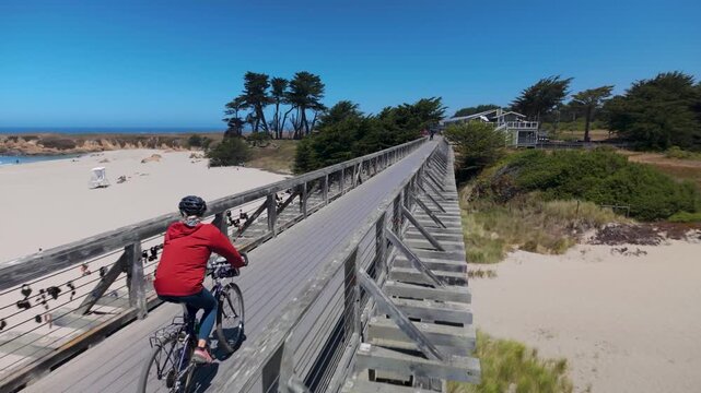 Mature woman rides her bike on Pudding Creek trestle bridge in Fort Bragg, enjoying the sunny weather and beautiful surroundings.