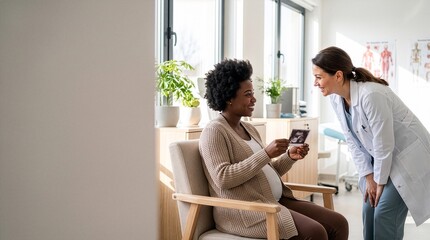 Obraz premium Smiling pregnant Black woman showing ultrasound scan photo to happy female doctor in bright medical clinic