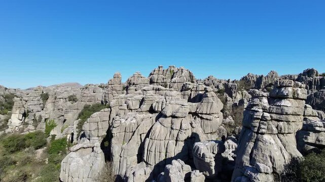 Drone aerial shot capturing massive layered limestone rock formations at Spain El Torcal Alto, with sparse vegetation under a clear blue sky.