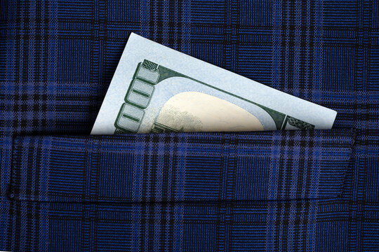 Close-up of a US hundred dollar bill partially visible in a blue plaid pocket, symbolizing savings, finance, or personal wealth.
