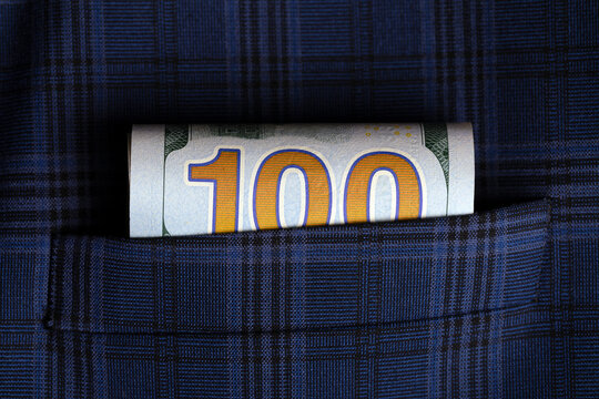 Rolled one hundred dollar bill tucked into a blue plaid suit pocket, symbolizing wealth, finance, and success.