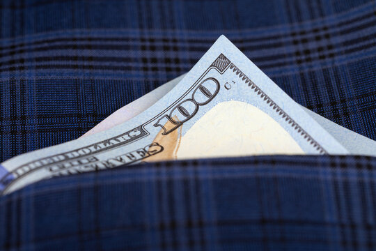 A crisp one hundred dollar bill partially visible in the pocket of a blue plaid fabric, symbolizing wealth, savings, and finance.