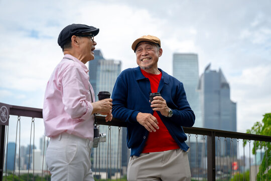Happy Senior Asian Men Drinking Coffee on Rooftop Terrace, Modern City Skyline Background