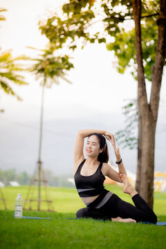 Young Asian woman practicing yoga outdoors in green park at sunrise