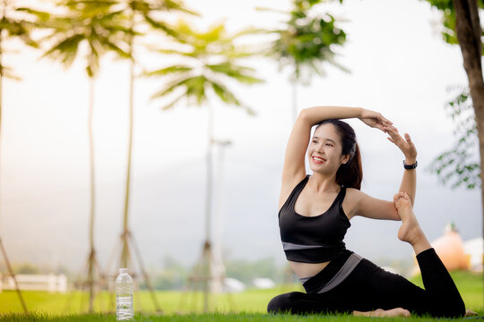 Young Asian woman practicing yoga outdoors in green park at sunrise